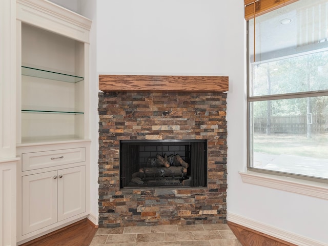 interior details with built in shelves, wood-type flooring, and a stone fireplace