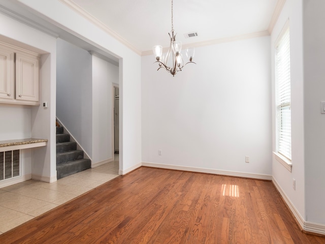 spare room featuring a wealth of natural light, light hardwood / wood-style flooring, crown molding, and a notable chandelier