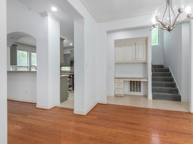 unfurnished living room with a chandelier, light wood-type flooring, and ornamental molding