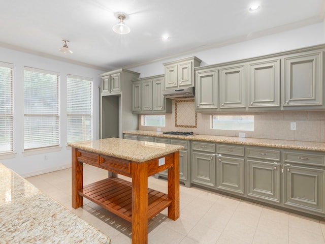 kitchen featuring light stone counters, light tile patterned floors, backsplash, stainless steel gas stovetop, and crown molding