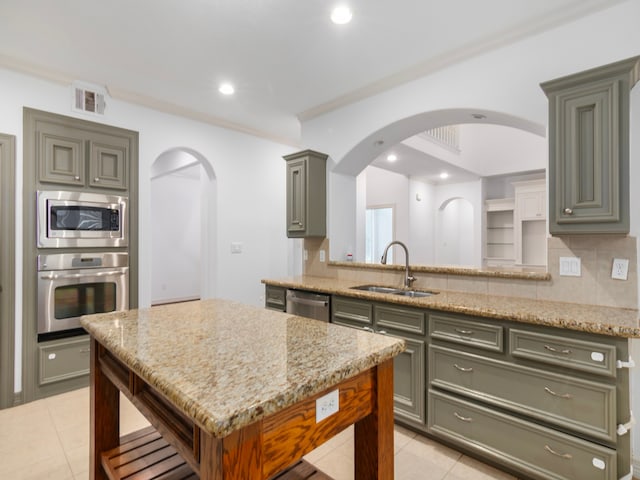 kitchen with stainless steel appliances, backsplash, light tile patterned floors, light stone countertops, and sink