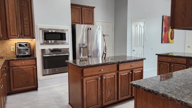 kitchen featuring dark stone counters, decorative backsplash, a kitchen island, and stainless steel appliances