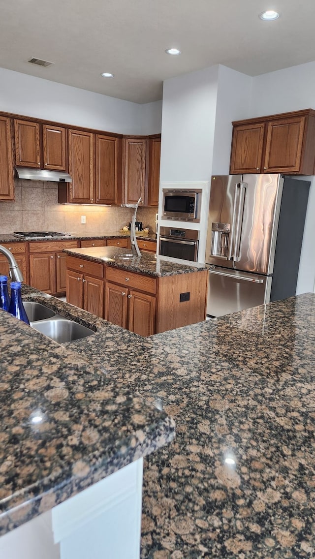 kitchen with sink, dark stone countertops, backsplash, and appliances with stainless steel finishes