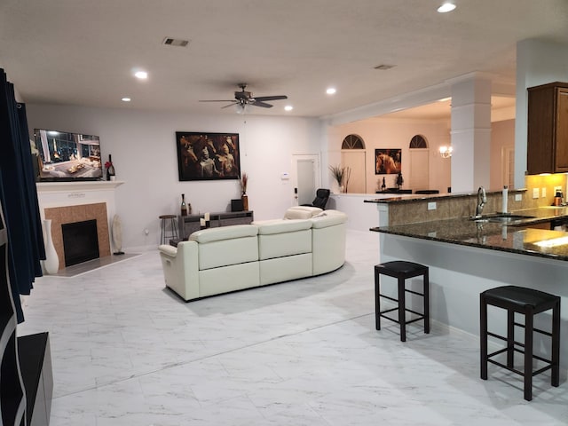 living room featuring a tiled fireplace, ceiling fan, and sink