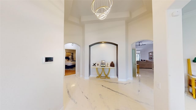 corridor featuring arched walkways, a notable chandelier, marble finish floor, and a towering ceiling