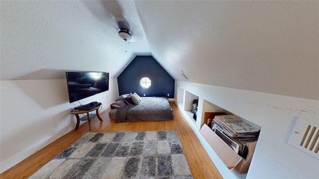 bedroom with ceiling fan, a textured ceiling, lofted ceiling, and wood finished floors