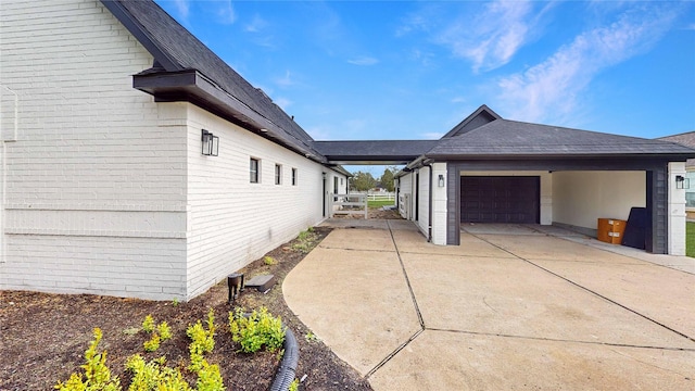 view of side of property with an attached garage, brick siding, driveway, and a shingled roof