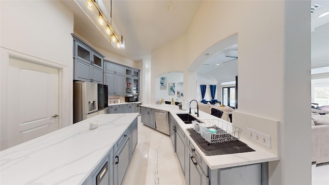 kitchen with arched walkways, a sink, stainless steel appliances, gray cabinetry, and glass insert cabinets