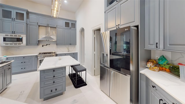 kitchen featuring tasteful backsplash, light stone countertops, wall chimney range hood, and appliances with stainless steel finishes