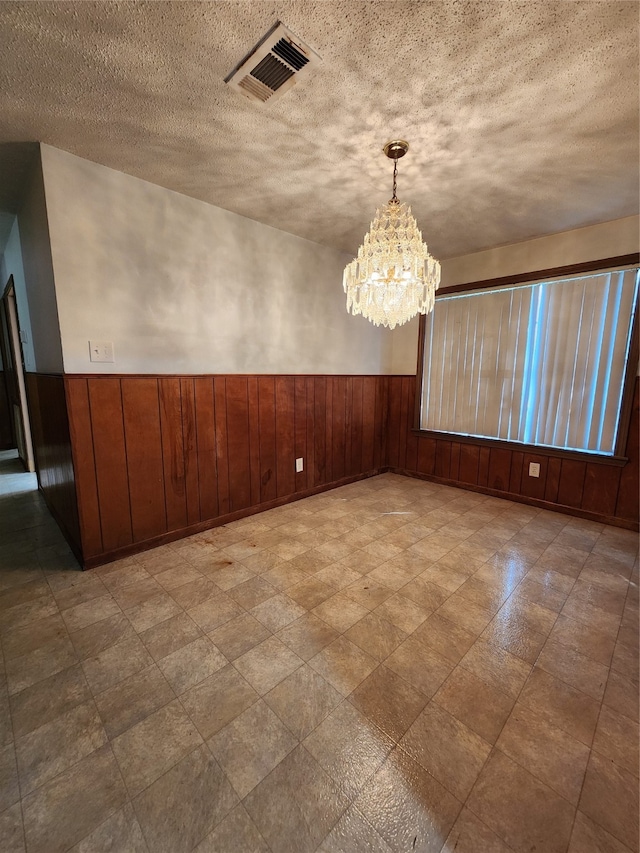 unfurnished dining area with wooden walls, a textured ceiling, and a chandelier