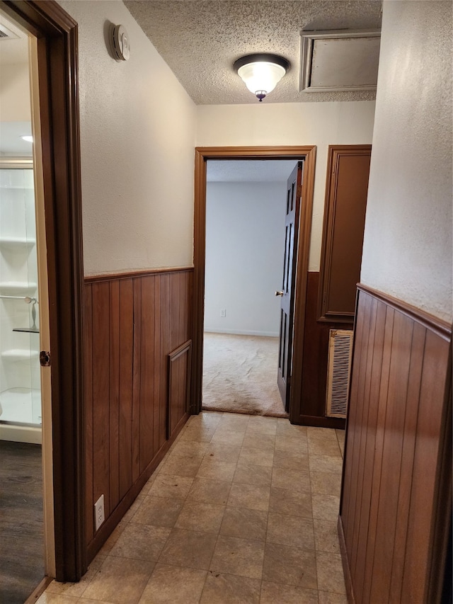 hall with wooden walls, a textured ceiling, and light colored carpet