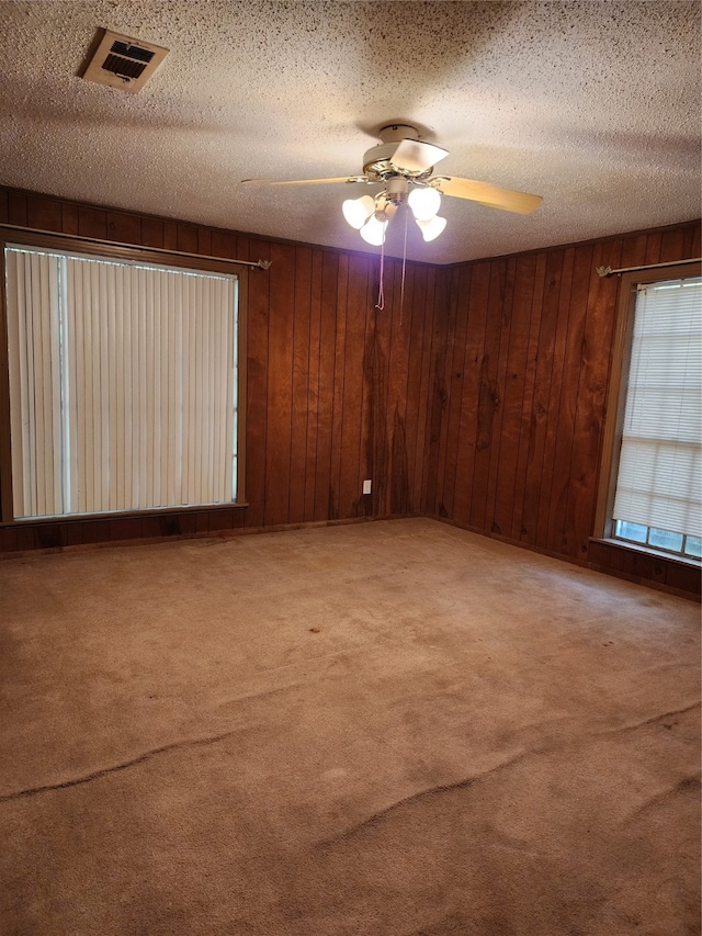 spare room featuring a textured ceiling, carpet floors, wooden walls, and ceiling fan