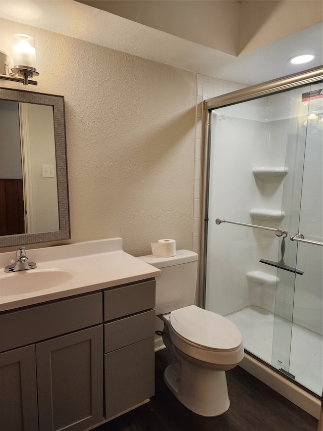 bathroom featuring toilet, vanity, hardwood / wood-style flooring, and a shower with door