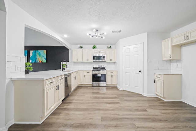 kitchen with stainless steel appliances, light hardwood / wood-style floors, kitchen peninsula, a textured ceiling, and backsplash