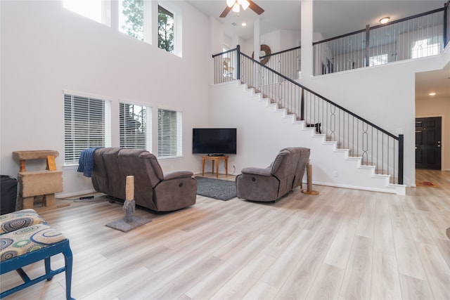 living room with a towering ceiling, light hardwood / wood-style flooring, and ceiling fan