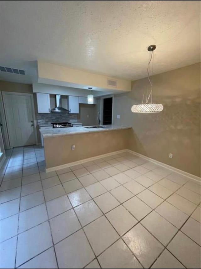 kitchen with decorative light fixtures, light tile patterned floors, white cabinets, kitchen peninsula, and wall chimney exhaust hood