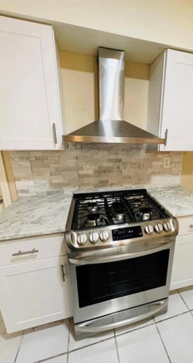 kitchen with white cabinets, wall chimney exhaust hood, light tile patterned floors, and stainless steel gas range