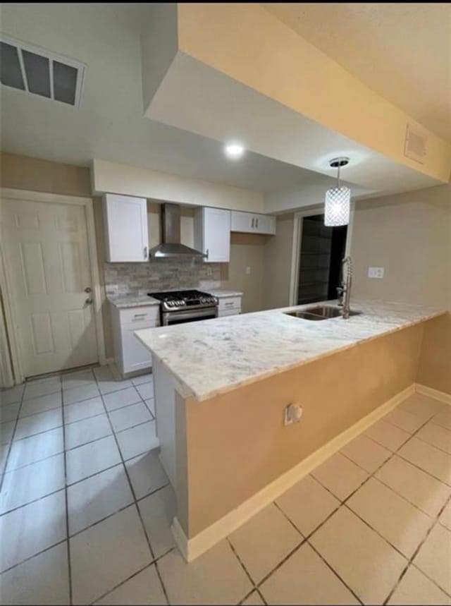 kitchen with white cabinetry, wall chimney range hood, stainless steel gas range oven, pendant lighting, and sink