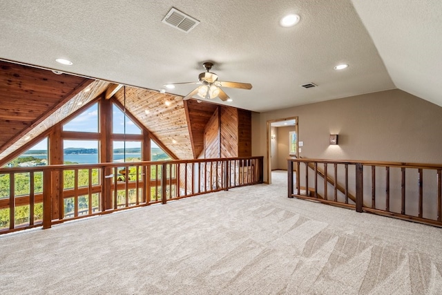 additional living space with visible vents, light colored carpet, a water view, vaulted ceiling, and recessed lighting