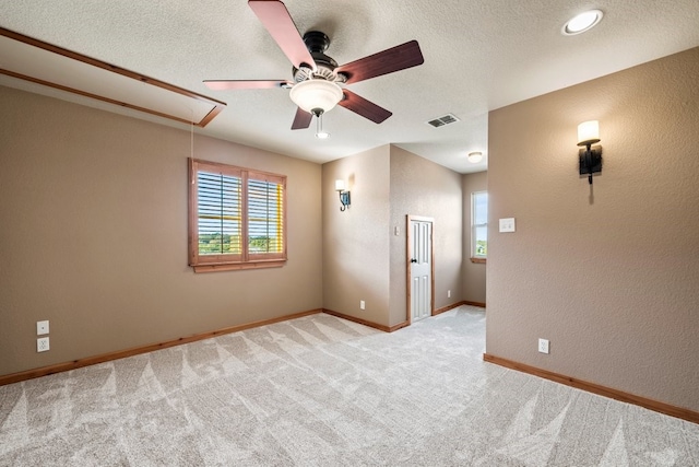 spare room with attic access, baseboards, visible vents, light colored carpet, and a textured ceiling