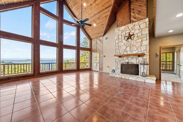 unfurnished living room with visible vents, a ceiling fan, tile patterned floors, a water view, and a stone fireplace