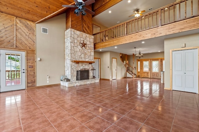 unfurnished living room with visible vents, tile patterned floors, wood walls, a fireplace, and ceiling fan with notable chandelier