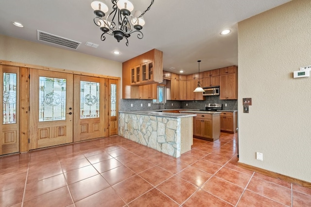 kitchen featuring brown cabinets, stainless steel appliances, visible vents, hanging light fixtures, and a peninsula