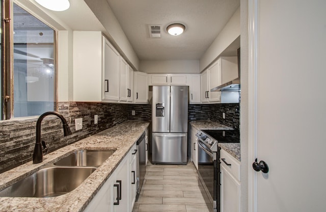 kitchen featuring wall chimney exhaust hood, appliances with stainless steel finishes, light stone counters, white cabinetry, and a sink