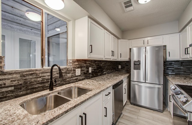 kitchen with visible vents, light stone countertops, stainless steel appliances, white cabinetry, and a sink