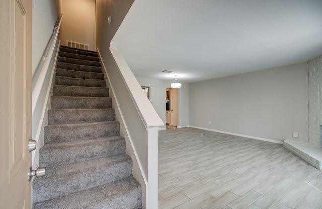 stairway with a brick fireplace, wood finished floors, visible vents, and baseboards