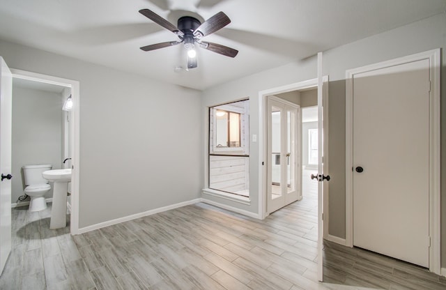 unfurnished bedroom with baseboards, a ceiling fan, ensuite bath, french doors, and light wood-type flooring