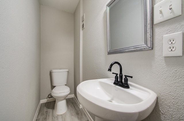 half bathroom featuring a textured wall, toilet, a sink, wood finished floors, and baseboards