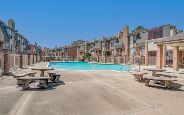 community pool with a patio area, fence, and a residential view