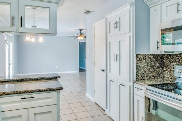 kitchen with backsplash, electric stove, light tile patterned floors, dark stone countertops, and white cabinetry