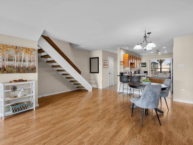 dining room with ceiling fan with notable chandelier and light hardwood / wood-style flooring