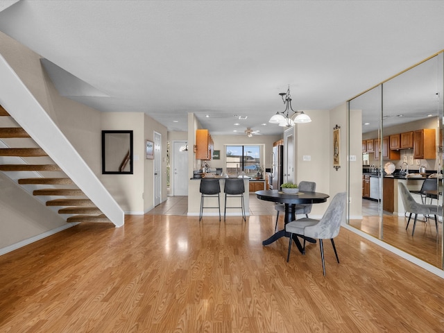 dining area with ceiling fan with notable chandelier and light hardwood / wood-style flooring