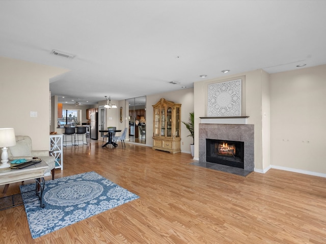 living room featuring an inviting chandelier, a tile fireplace, and light hardwood / wood-style flooring