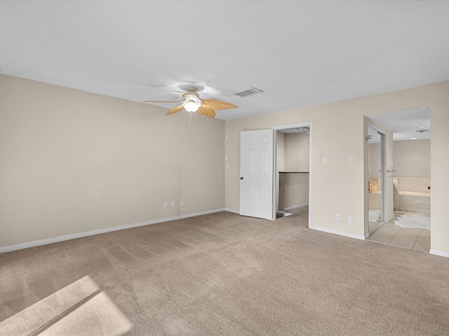 unfurnished bedroom featuring ceiling fan, connected bathroom, a walk in closet, and light colored carpet