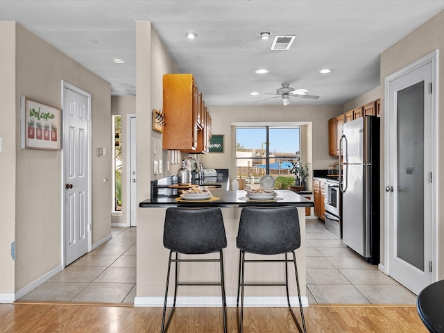 kitchen with a breakfast bar, ceiling fan, light wood-type flooring, and appliances with stainless steel finishes