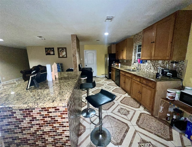 kitchen featuring decorative backsplash, light stone counters, a breakfast bar, sink, and dishwasher