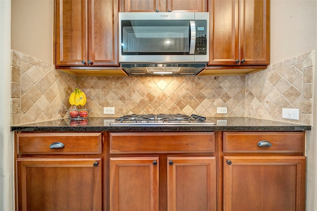 kitchen with appliances with stainless steel finishes, dark stone counters, and backsplash