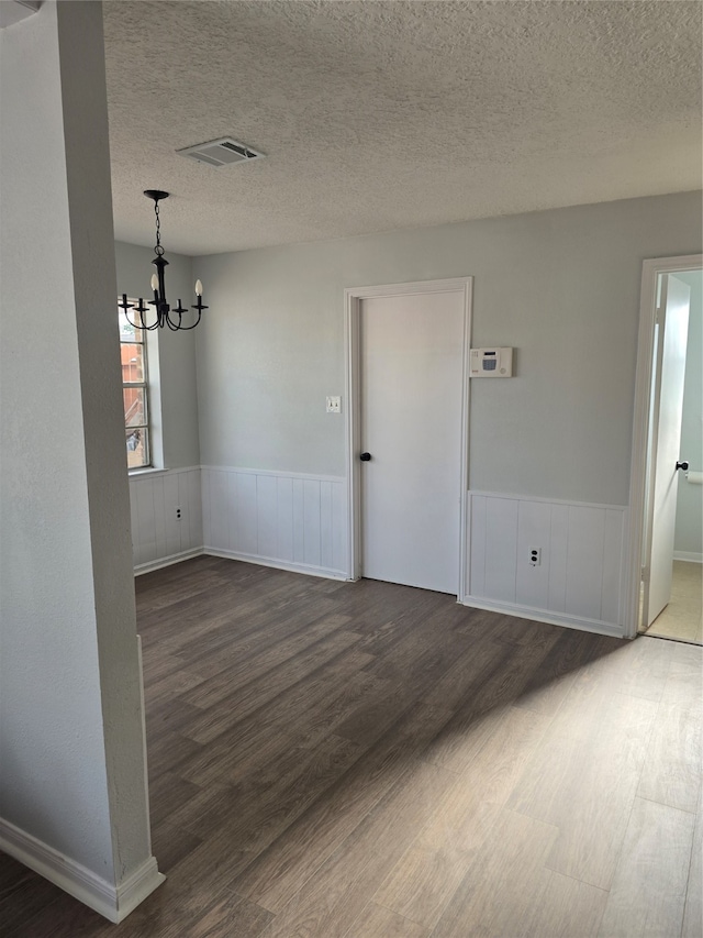 spare room with dark wood-type flooring, a textured ceiling, and a notable chandelier