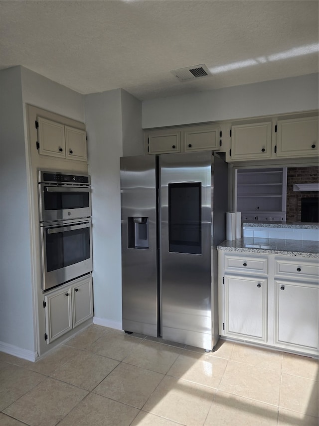 kitchen with light stone countertops, light tile patterned floors, stainless steel appliances, and a textured ceiling