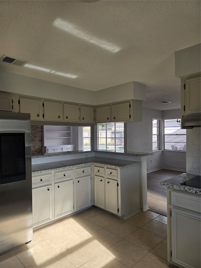 kitchen featuring light stone countertops, a textured ceiling, light tile patterned floors, tasteful backsplash, and kitchen peninsula