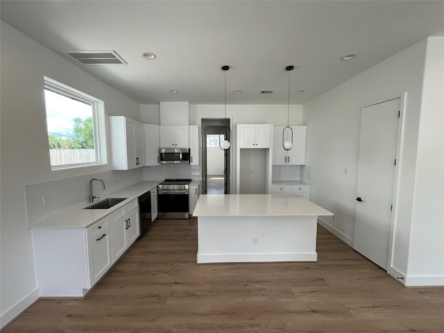 kitchen with white cabinetry, a center island, sink, stainless steel appliances, and decorative light fixtures