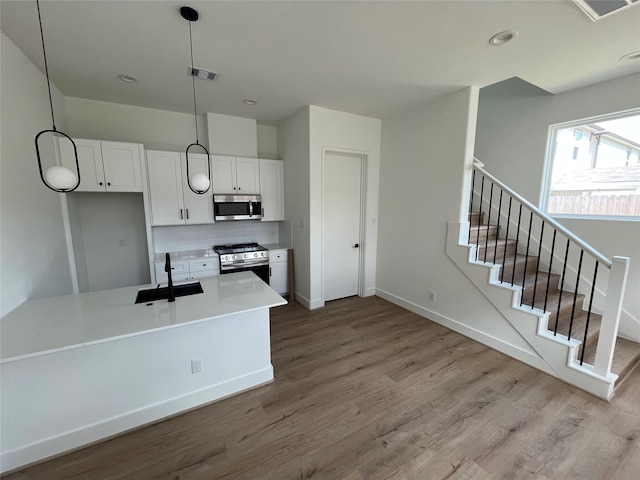 kitchen featuring stainless steel appliances, backsplash, pendant lighting, white cabinets, and light wood-type flooring