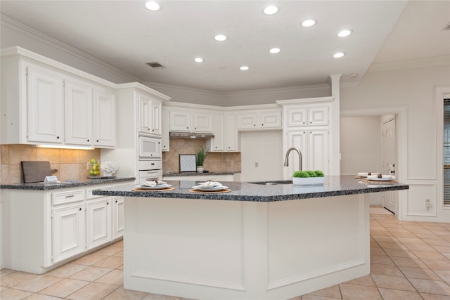 kitchen with white cabinetry, ornamental molding, light tile patterned floors, white appliances, and a kitchen island with sink