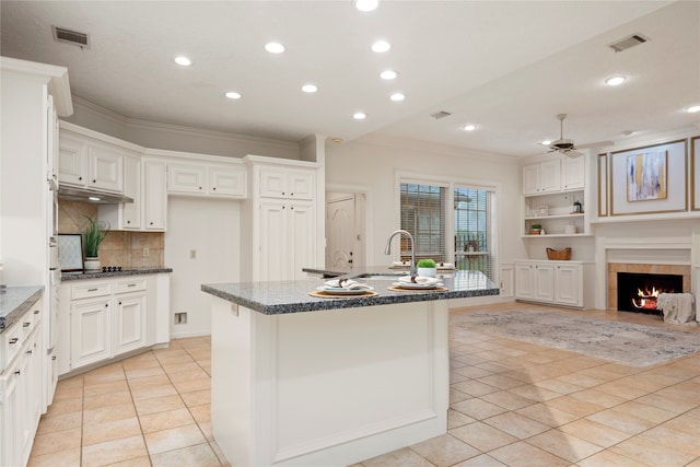 kitchen with a tiled fireplace, dark stone countertops, sink, and a kitchen island with sink