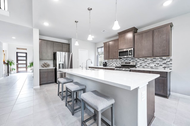 kitchen featuring dark brown cabinetry, a kitchen island with sink, appliances with stainless steel finishes, and decorative light fixtures