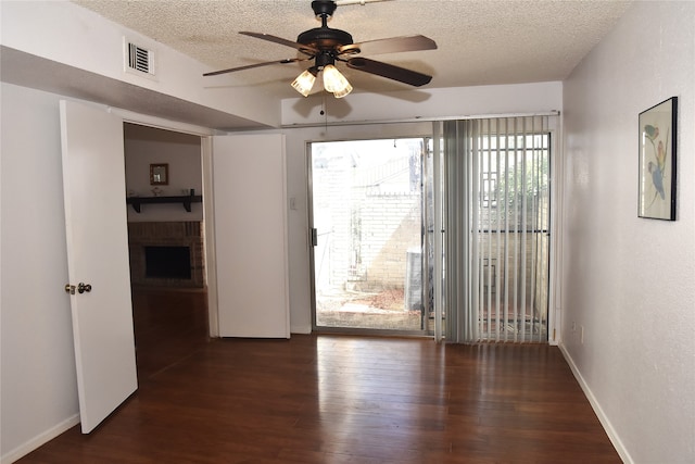 unfurnished room featuring ceiling fan, a textured ceiling, dark hardwood / wood-style floors, and a fireplace